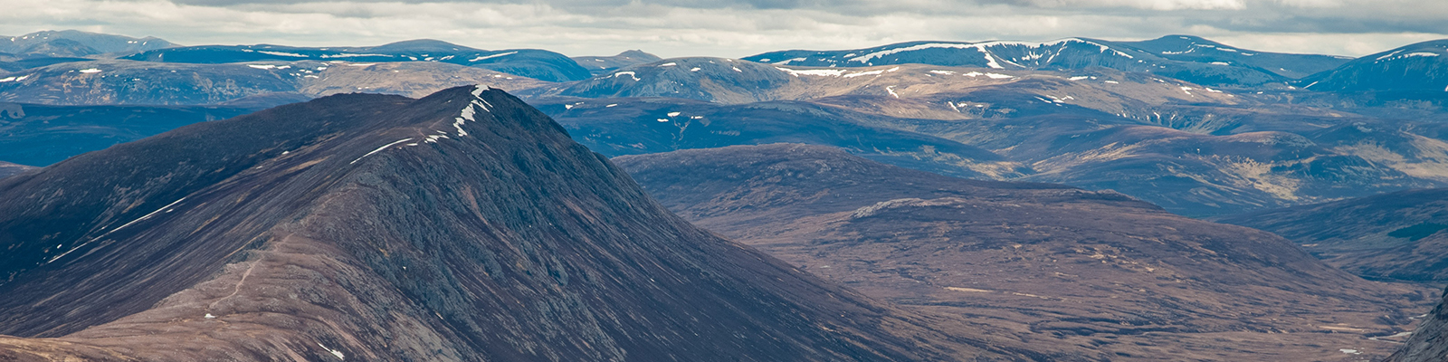 Vista of Scottish mountains and valleys with remnants of snow on the peaks and high areas. Grey, cloudy sky