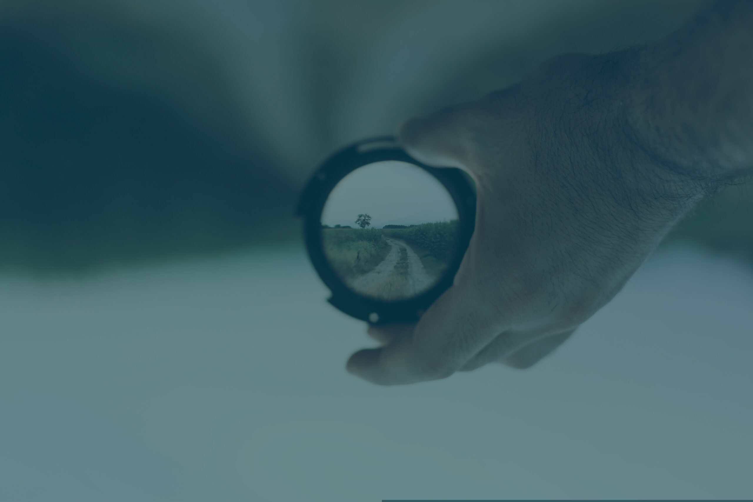 Career clarity in marketing represented by a camera lens held in a hand and looking at a blurred vista. Through the lens a country path can be seen in focus